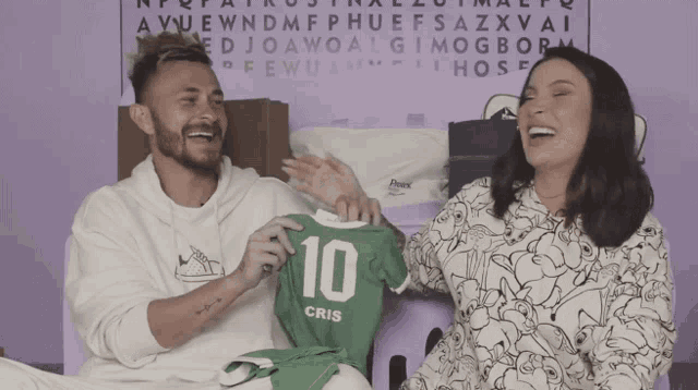 a man and a woman are laughing while holding a green jersey with the number 10 on it