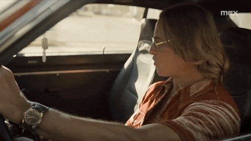 a man wearing glasses is driving a car with the word mox on the bottom