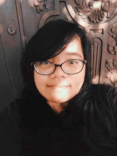 a woman wearing glasses is smiling in front of a carved wooden door