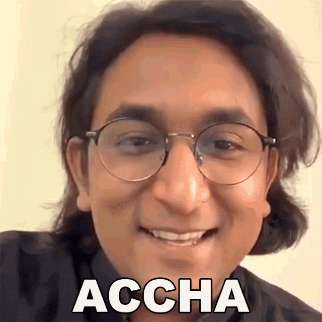 a man wearing glasses and a black shirt has the word accha written on his face