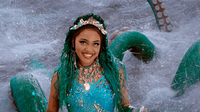 a woman with green hair and a crown is standing in the water with an octopus behind her .