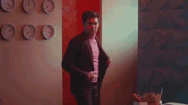 a man in a suit is standing in a room with clocks on the wall and talking on a cell phone .