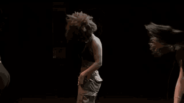 a woman with afro hair is dancing in a dark room with other women .