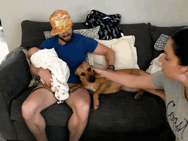 a man is holding a baby while a woman petting a dog on a couch