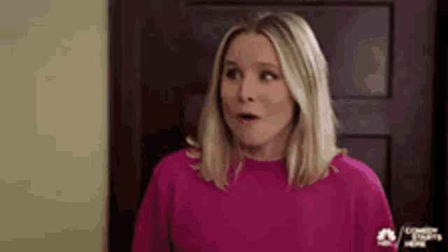a woman is wearing a pink sweater and making a surprised face .