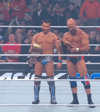 two wrestlers standing in a ring with a royal rumble sign in the back
