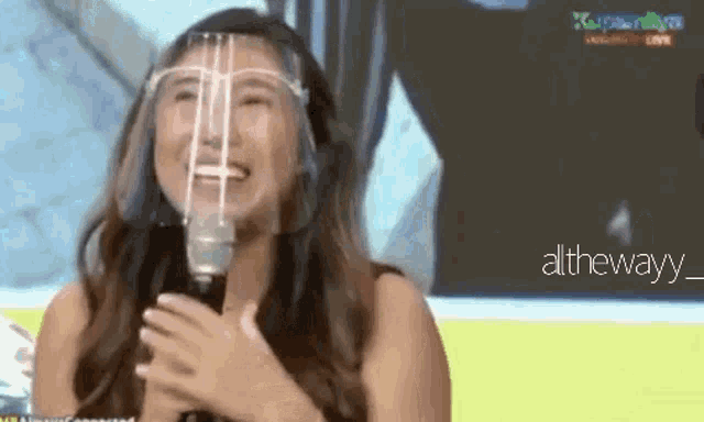 a woman wearing a face shield is laughing while holding a microphone .