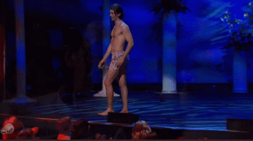a man without a shirt is standing on a stage with a crowd watching