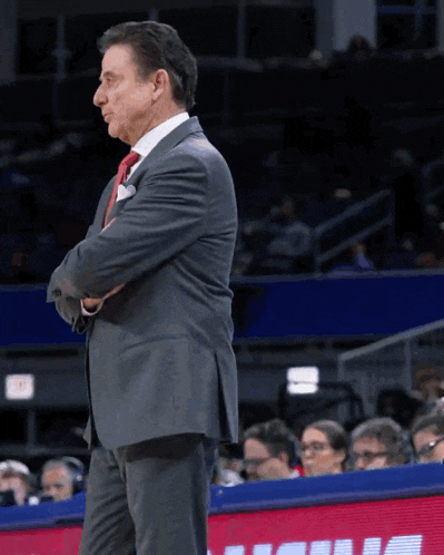 a man in a suit and tie stands on a basketball court with his arms crossed