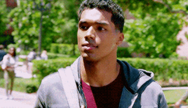 a young man wearing a gray jacket and a red shirt is walking down a sidewalk .