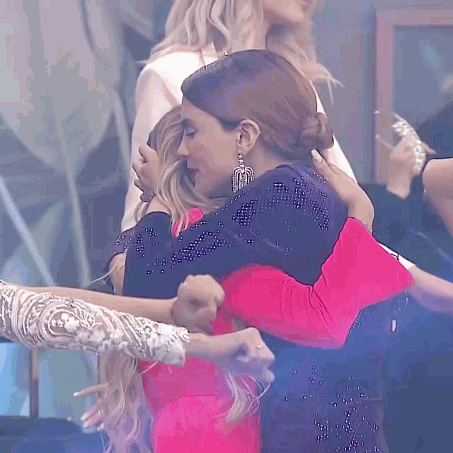 a woman in a pink dress is hugging another woman