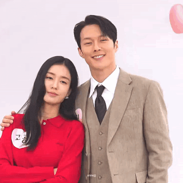 a man in a suit and tie is standing next to a woman in a red shirt
