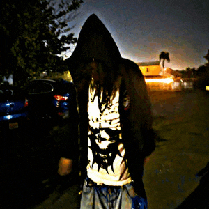 a man wearing a hoodie and a shirt with a skull on it stands in a dark parking lot