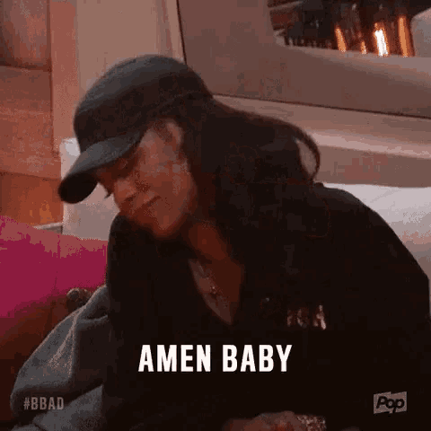 a woman in a baseball cap is sitting on a couch and says amen baby .