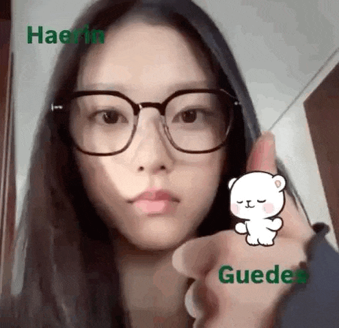 a woman wearing glasses is giving a thumbs up sign with a cartoon bear on her finger .