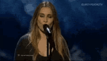 a woman is singing into a microphone with eurovision tv in the background