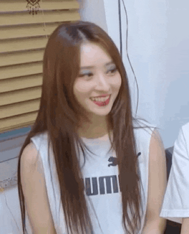 a young woman with long hair is smiling and wearing a white tank top .