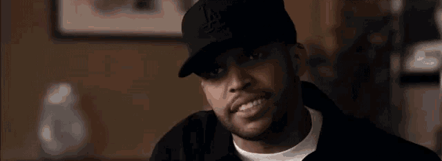 a man wearing a black hat and a white shirt is sitting in a room .