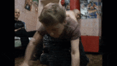 a man is laying on another man 's back in a room with a boxing poster on the wall