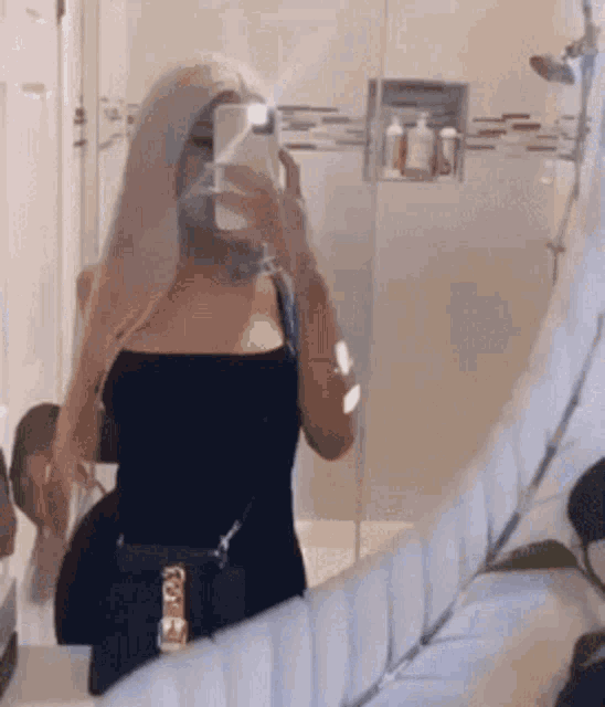 a woman is taking a selfie in a bathroom mirror with her phone .
