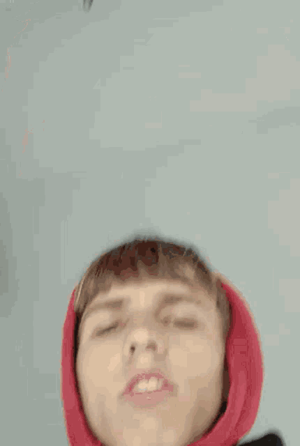 a young man wearing a red hoodie is making a face