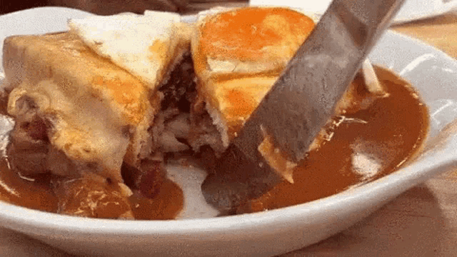 a person is cutting a sandwich with a knife on a plate of food .