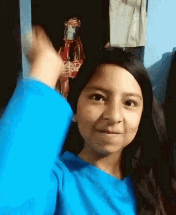 a young girl in a blue shirt is clapping her hands in front of a coke bottle .