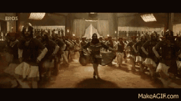 a woman is dancing in front of a large group of people in armor .