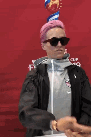 a woman with pink hair is wearing sunglasses and a jacket that says us