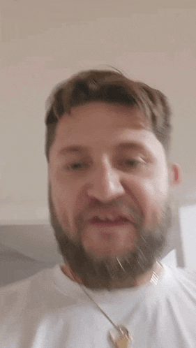 a man with a beard is wearing a white t-shirt and a gold necklace .