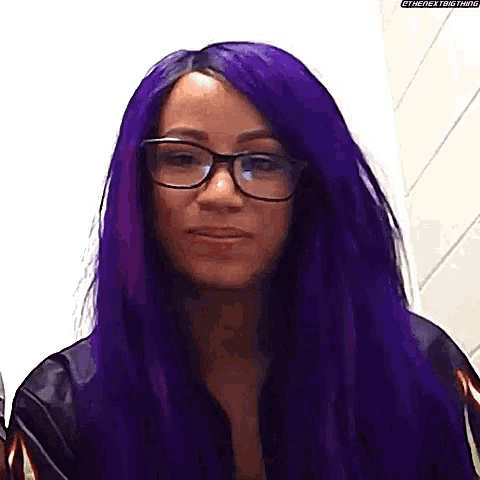 a woman with purple hair and glasses is wearing a black shirt .