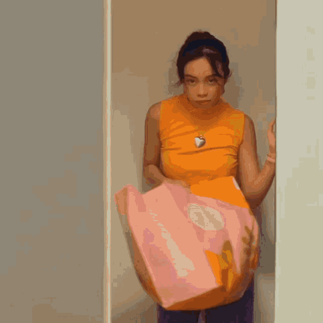a woman in an orange tank top is standing in a closet holding a pink and orange blanket .