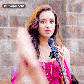 a woman is singing into a microphone while wearing a pink top .