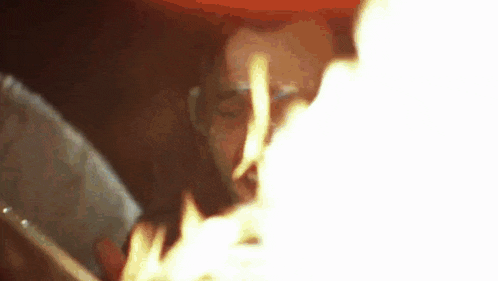 a man is smoking a cigarette in a dark room with a light coming out of his mouth .