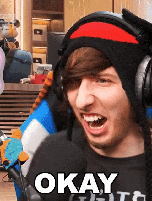 a man wearing a hat and headphones says okay in front of a microphone