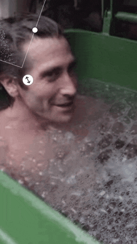 a man is taking a bath in a green tub with bubbles coming out of his head