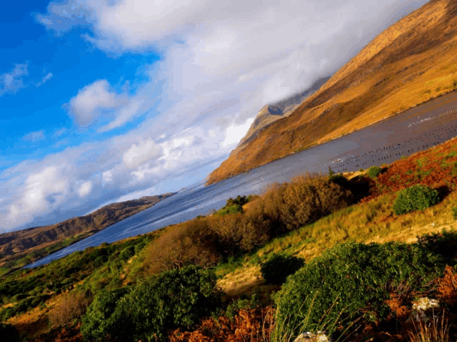 a lake surrounded by mountains and trees with a blue sky