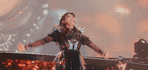 a woman in a metal outfit is dancing on a stage with her arms outstretched