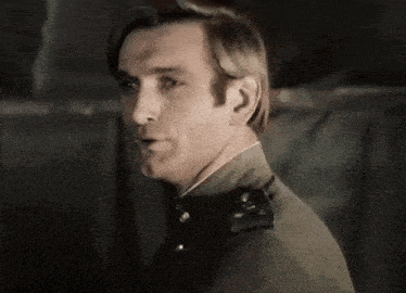 a man in a military uniform is standing in a dark room and looking at the camera .