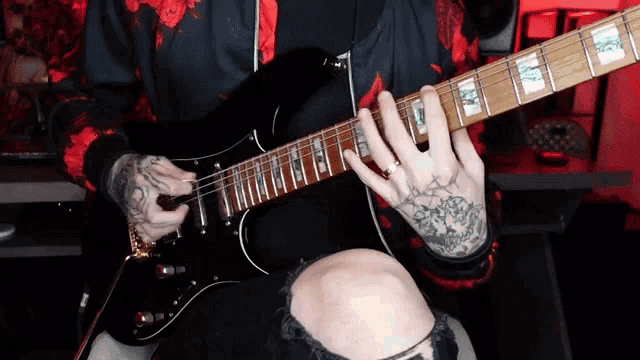 a person with tattoos on their hands is playing a guitar