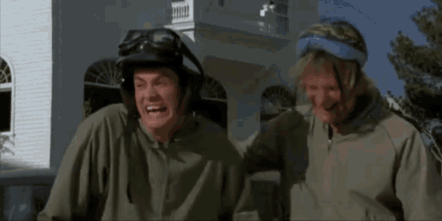 two men wearing helmets and goggles are standing next to each other in front of a house