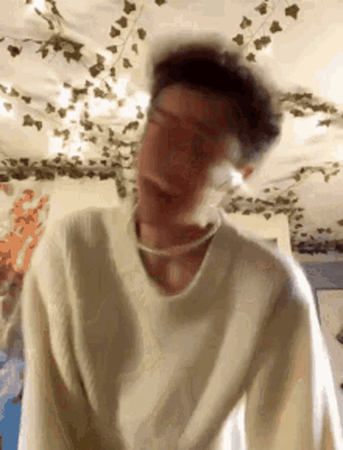 a man in a white sweater is making a funny face in a room with ivy on the ceiling .