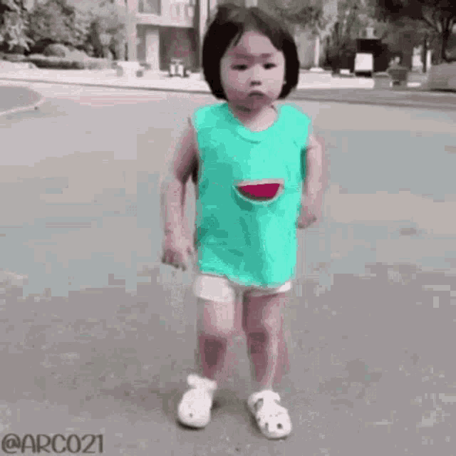a little girl in a watermelon shirt is walking down the street .