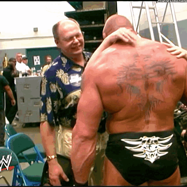 a man in a hawaiian shirt is hugging another man with a tattoo on his back