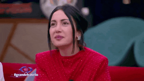 a woman in a red top is sitting on a red couch with a sign that says grandefratello on it