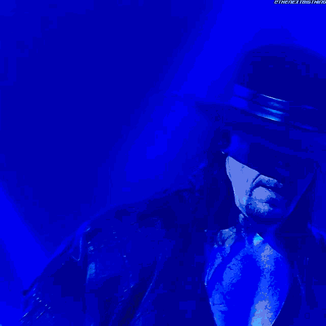 a man in a hat is standing in a dark room with a blue light behind him that says " thenextbigthing "