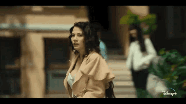 a woman is walking down a street in front of a building while a man stands in the background .