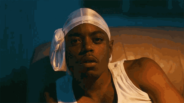 a man wearing a headband and a white tank top is sitting on a couch