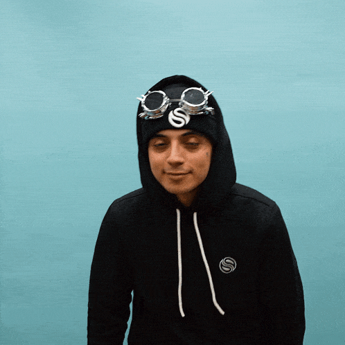a man wearing a black hoodie and a black beanie with the letter s on it