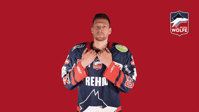 a man wearing a rehu jersey stands in front of a wolfe logo
